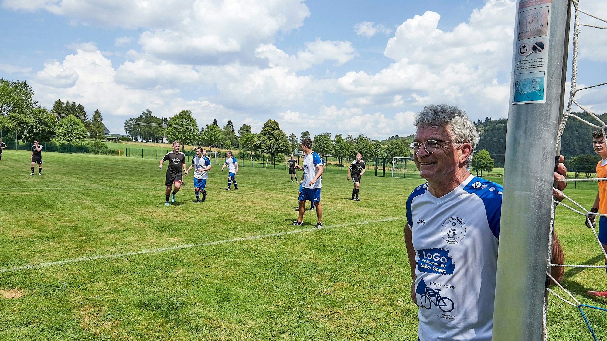 Egon Schmitz steht am Torpfosten, im Hintergrund Mitspieler und Spieler der gegnerischen Mannschaft.