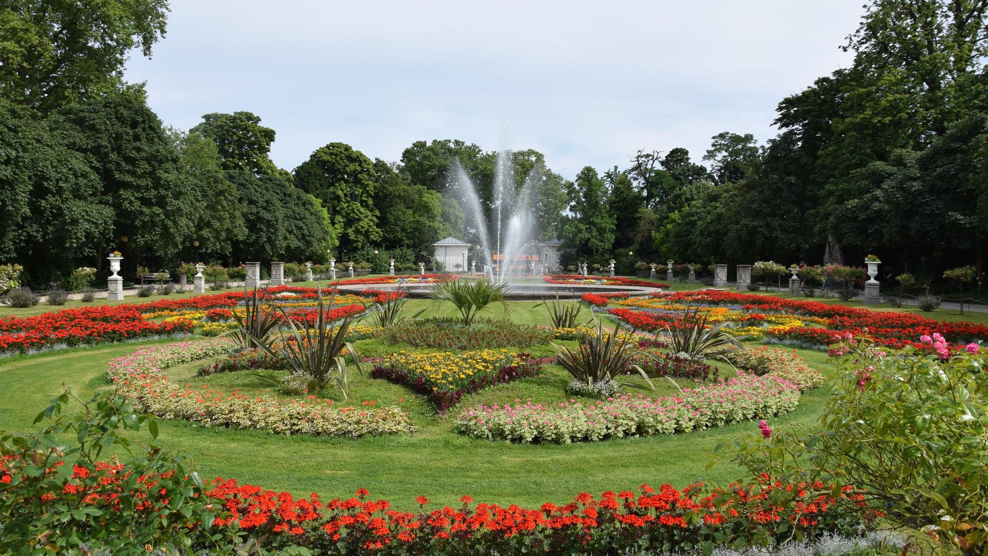 Der bunt blühende Vorgarten der Flora, mit seinen ordentlich angelegten Blumen und dem Brunnen.