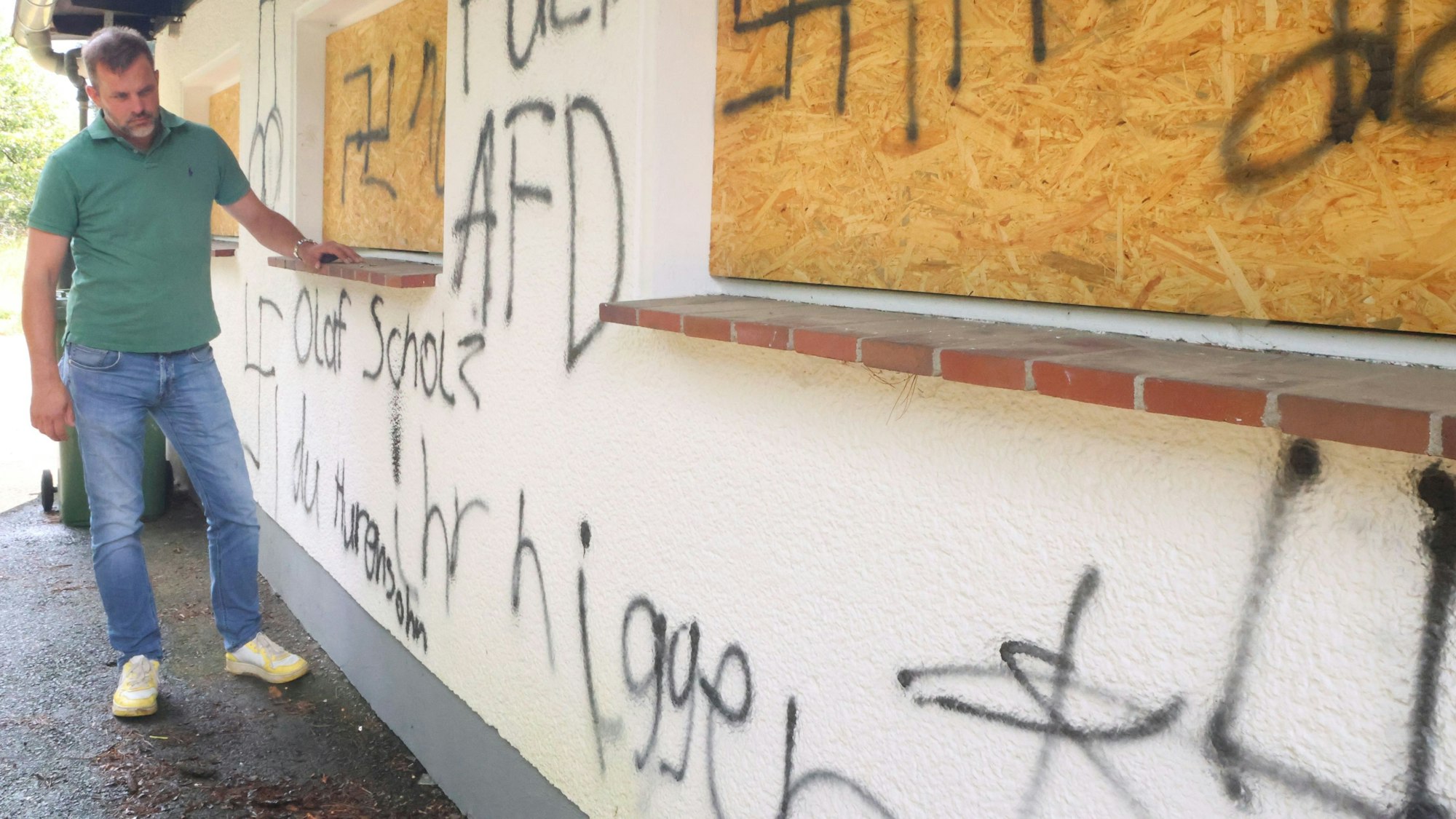 Der Waldbröler Unternehmer Michael Kappenstein steht an der beschmierten Wand seines Firmengebäudes an der Talstraße. Ein Anwohner hat ihm ein Foto zur Verfügung gestellt, das zwei Jugendliche beim Weglaufen zeigt.