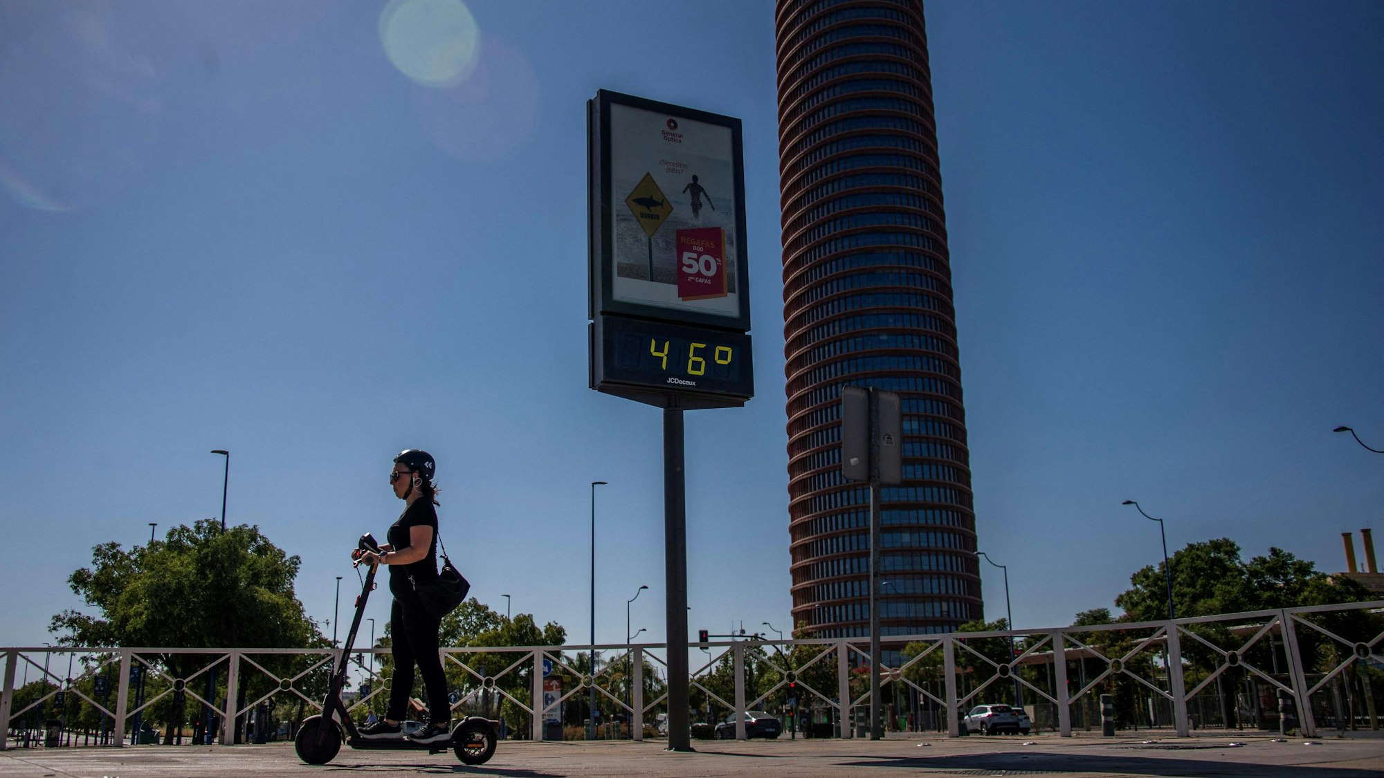 Eine Frau fährt auf einem E-Roller, im Hintergrund zeigt ein Thermometer 46 Grad an.