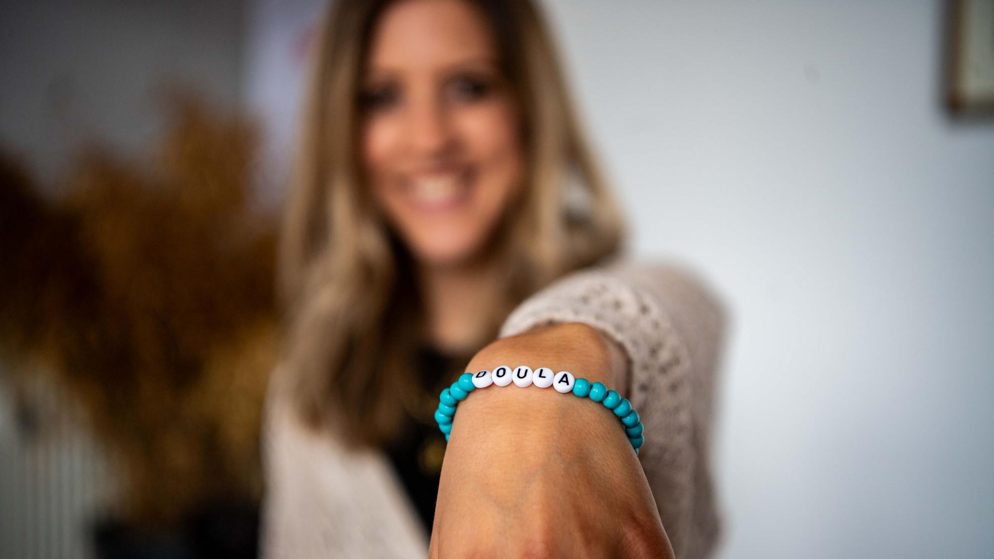 Das Bild zeigt Kerstin Blindert, die ein Armband mit der Aufschrift „Doula“ in die Kamera hält.