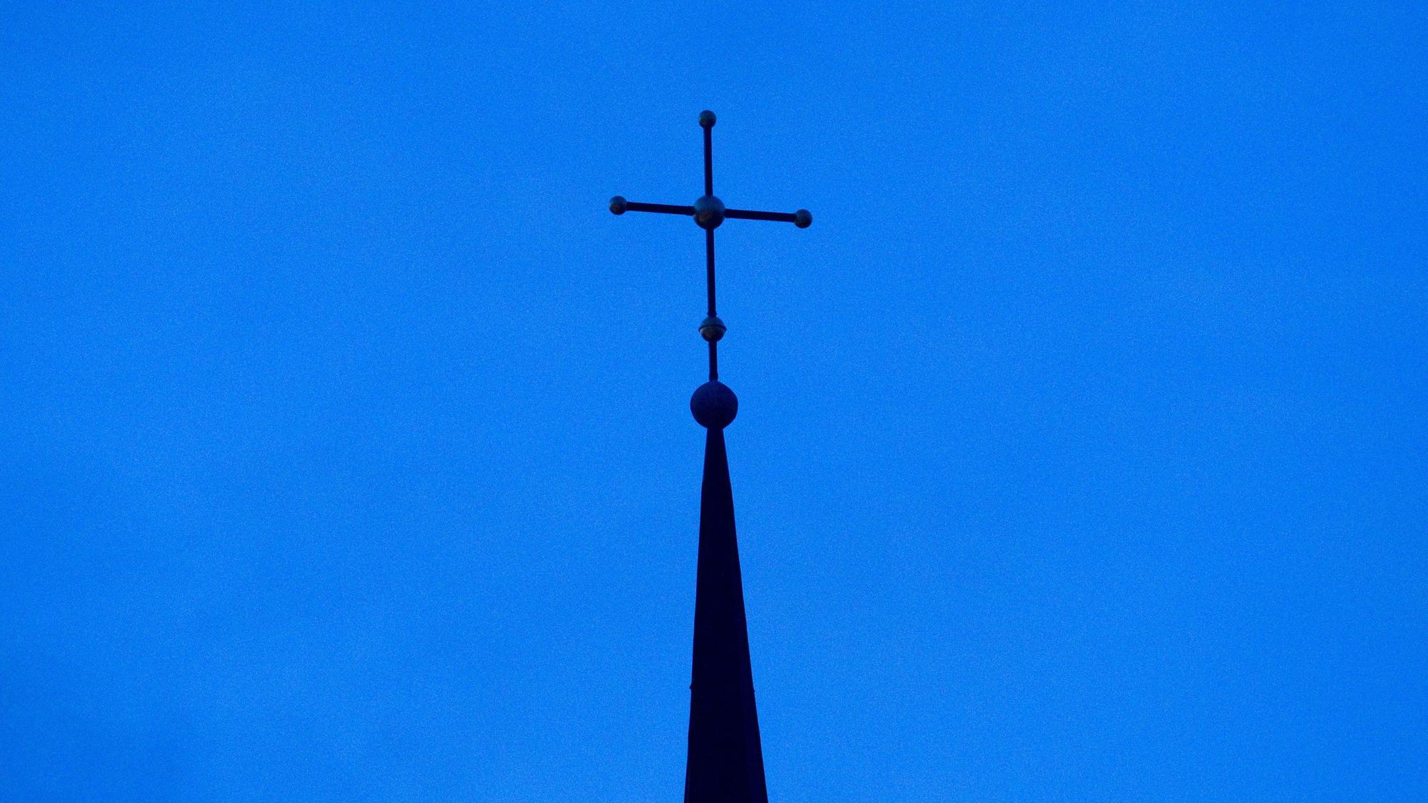 Das Kreuz einer Kirche ist in der Abenddämmerung zu sehen.