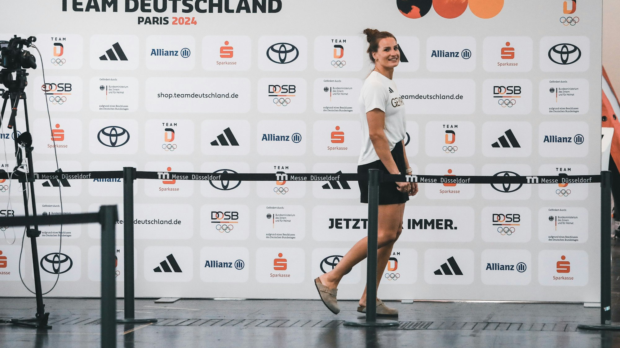 Anna-Maria Wagner, bekleidet in der Ausrüstung des deutschen Olympia-Teams, geht an einer Sponsorenwand entlang.