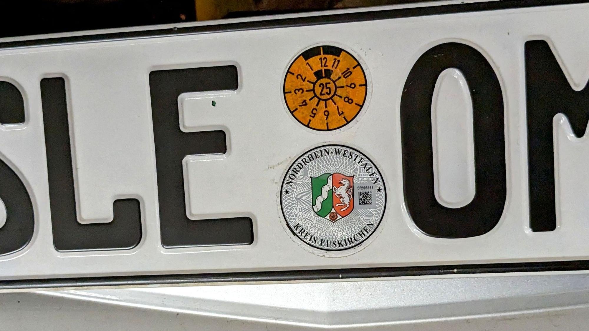Ein Autokennzeichen mit der Kennung SLE, HU-Plakette und Siegel des Kreises Euskirchen.