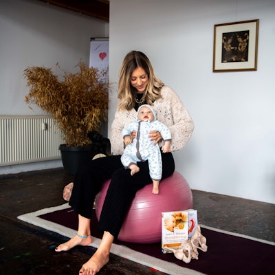 Das Bild zeigt Kerstin Blindert, auf einem Ball sitzend. Sie hat eine Puppe im Arm.