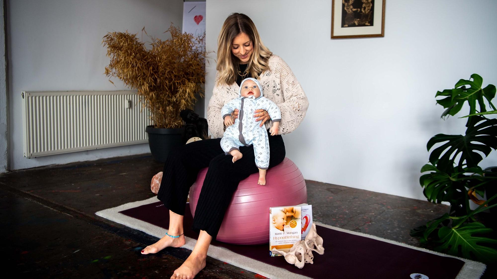 Das Bild zeigt Kerstin Blindert, auf einem Ball sitzend. Sie hat eine Puppe im Arm.