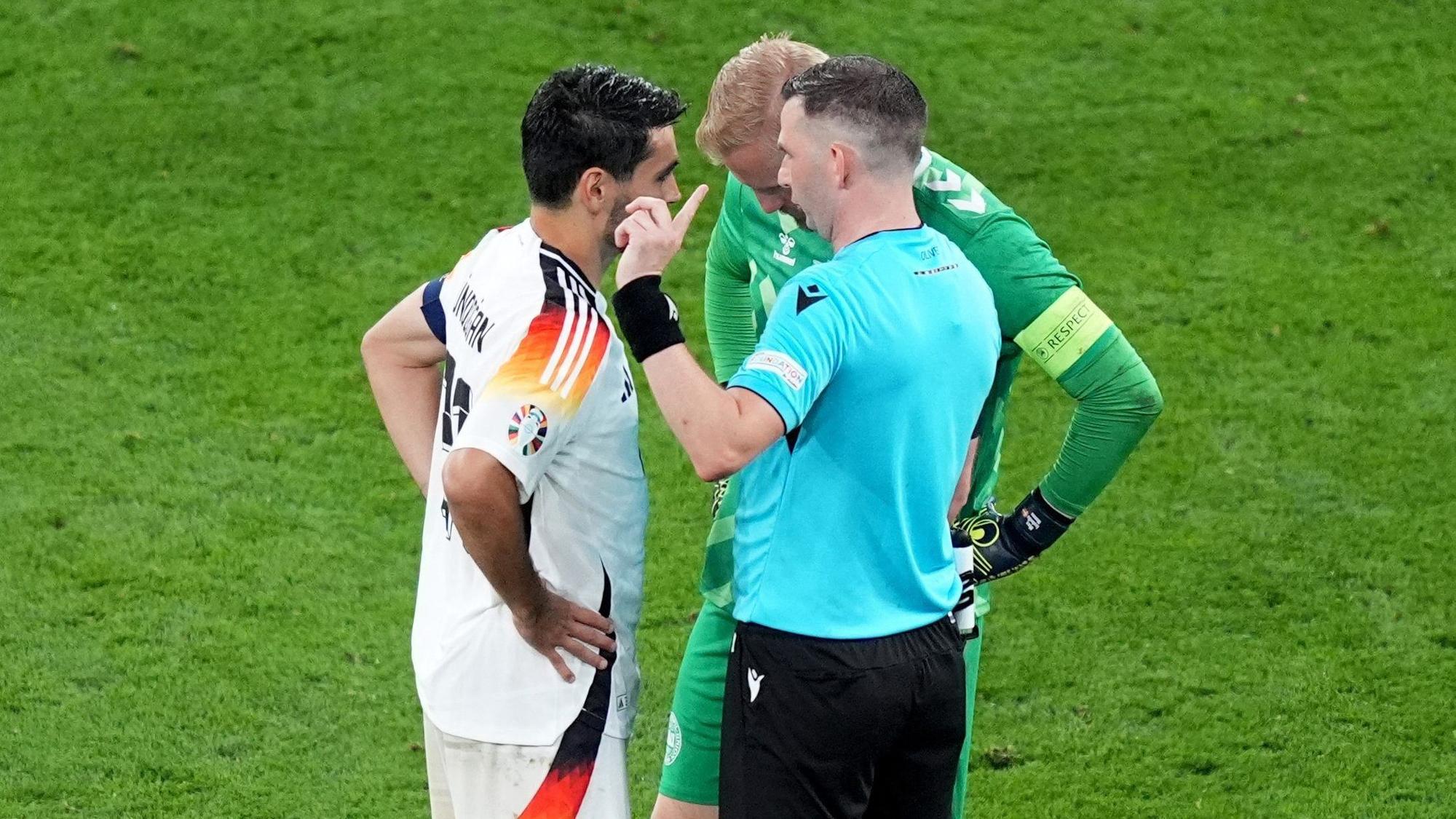 ARCHIV - 29.06.2024, Nordrhein-Westfalen, Dortmund: Fußball: EM, Deutschland - Dänemark, Finalrunde, Achtelfinale, Stadion Dortmund, Schiedsrichter Michael Oliver aus England spricht mit den beiden Kapitänen Ilkay Gündogan (l) und Dänemarks Kasper Schmeichel. (zu dpa: «Schiri-Chef fordert einheitliche Anwendung der Kapitänsregel») Foto: Marcus Brandt/dpa +++ dpa-Bildfunk +++