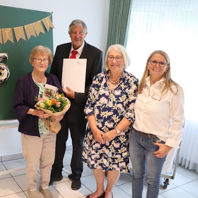 Gruppenfoto mit einer 150 aus Luftballons im Hintergrund. Eine ältere Frau, die Geburtstag hat, hält einen Blumenstrauß in den Händen.