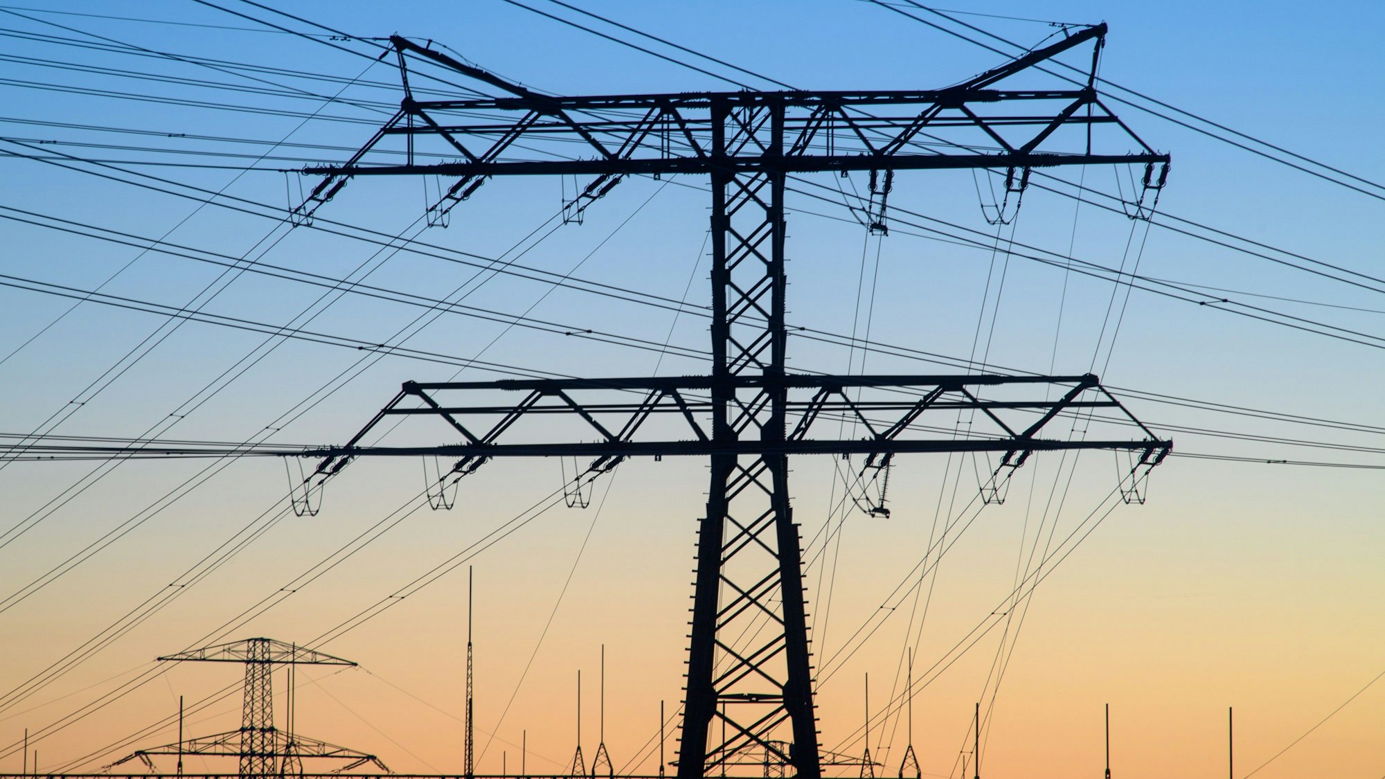 Strommasten und Stromleitungen im Morgengrauen bei dunstigem Licht.