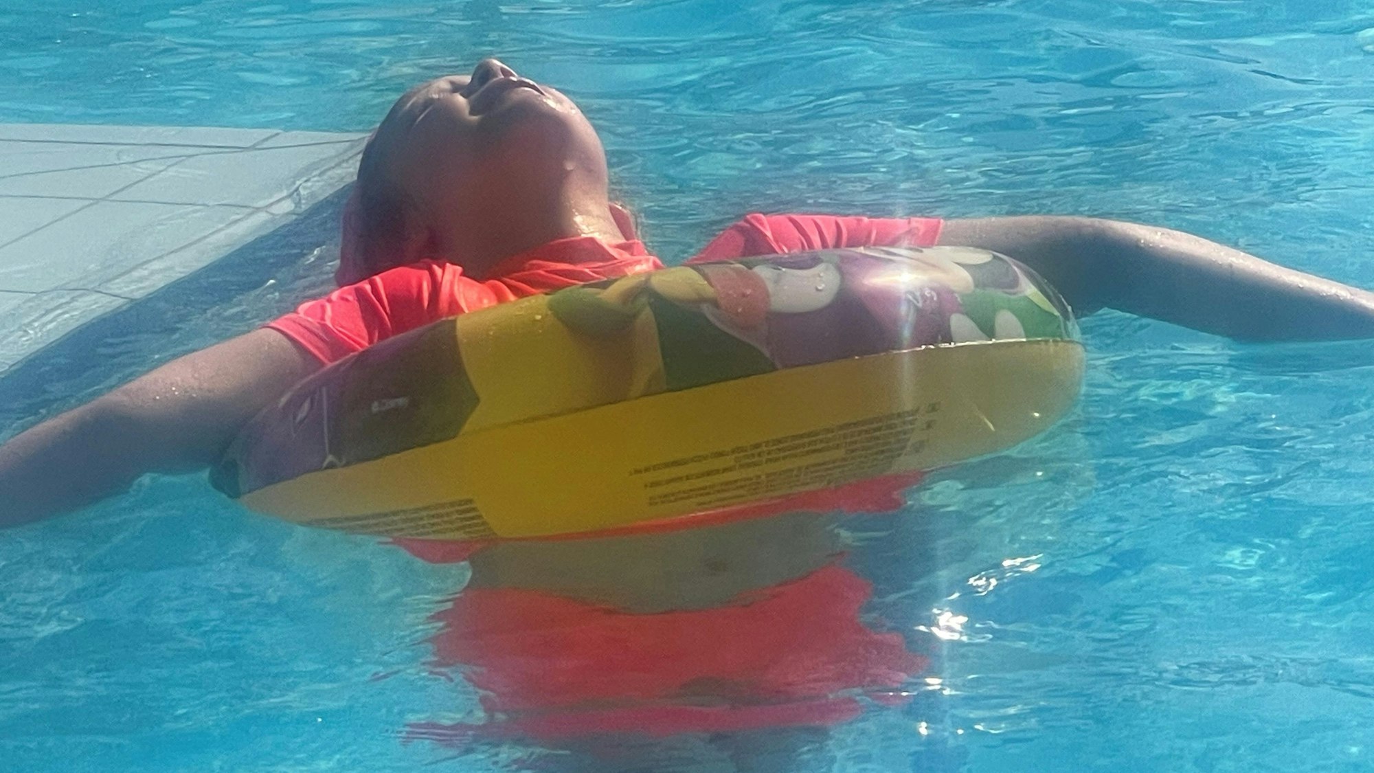 Das Bild zeigt ein Mädchen, das in einem Schwimmreifen auf dem Wasser treibt und die Sonne genießt.