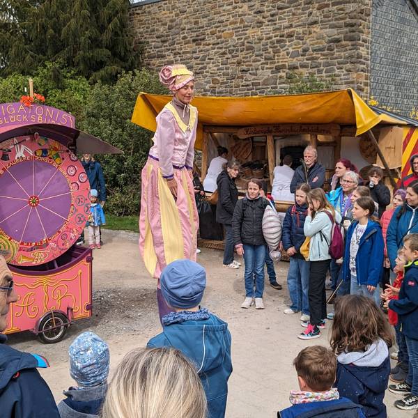 Das Publikum staunt über auf Stelzen gehende Akteure, die Betreiber eines Jahrmarkts aus früheren Jahrhunderten darstellen.