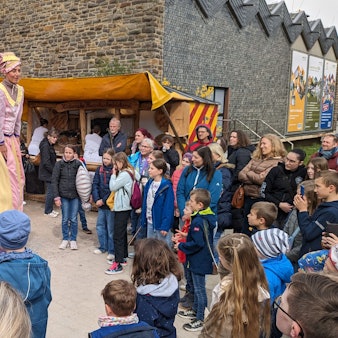 Das Publikum staunt über auf Stelzen gehende Akteure, die Betreiber eines Jahrmarkts aus früheren Jahrhunderten darstellen.