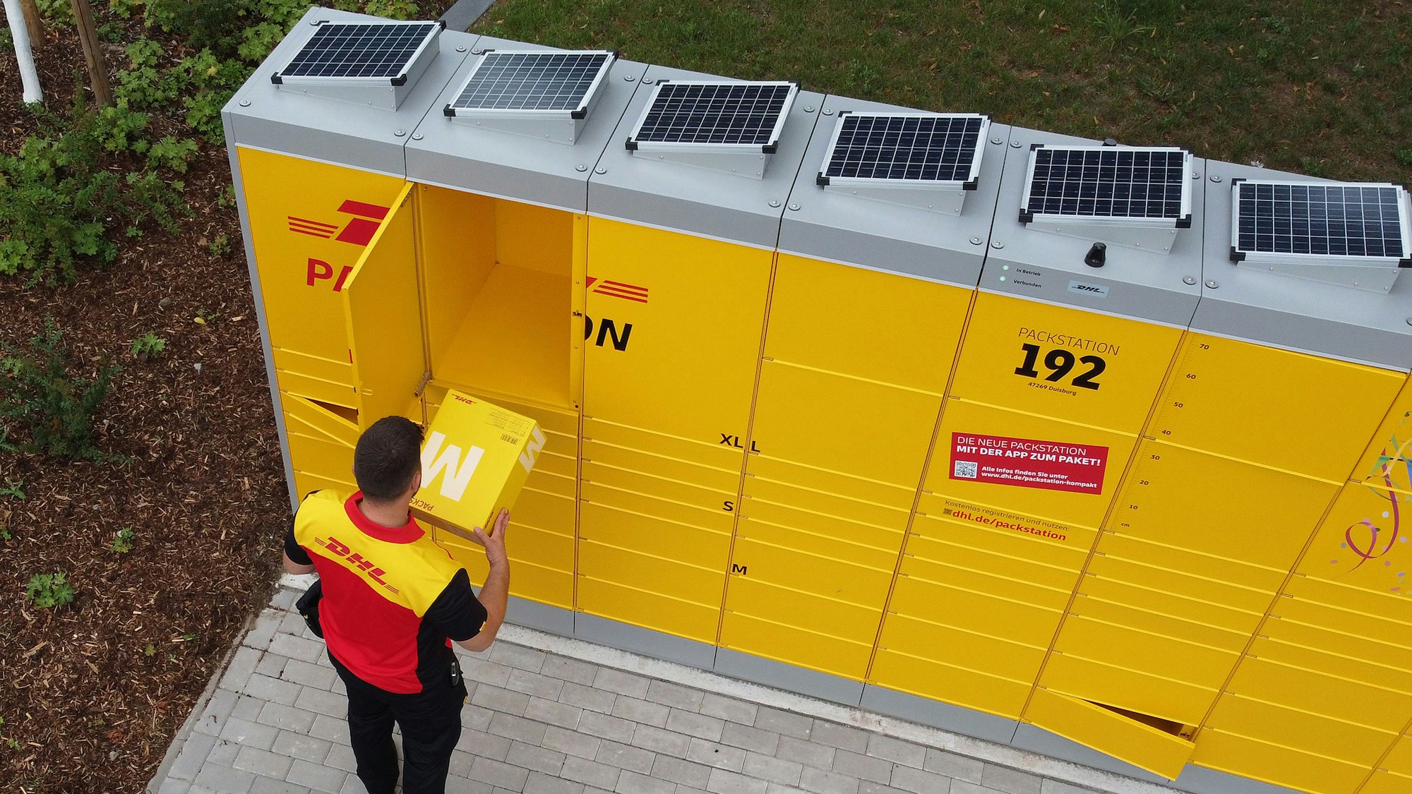 Ein Postbote packt ein Paket in eine solarbetriebene Packstation.