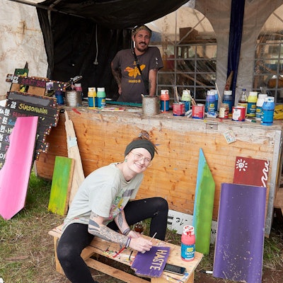 Ein Mann und eine Frau sind in einem Zelt, auf einer Theke stehen zahlreiche Farbtuben und -dosen. Sie gestalten die Hinweisschilder für das Zugvögel-Festival am Weißen Stein in Hellenthal-Udenbreth.