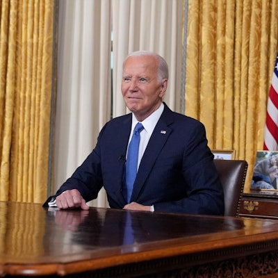 US-Präsident Joe Biden sitzt im Oval Office im Weißen Haus vor einer US-amerikanischen Flagge und blickt vor einer Rede in die Kamera.
