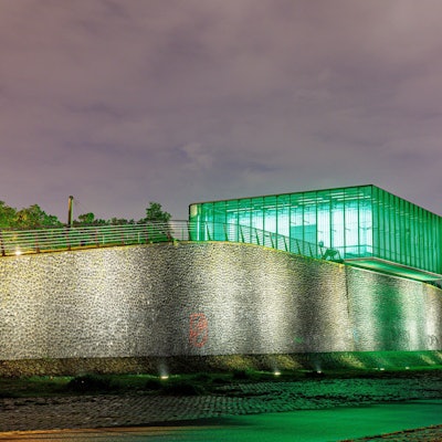 Ein grün leuchtender Baukörper steckt auf einer Rampe am Rheinufer und signalisiert den Wasserstand.