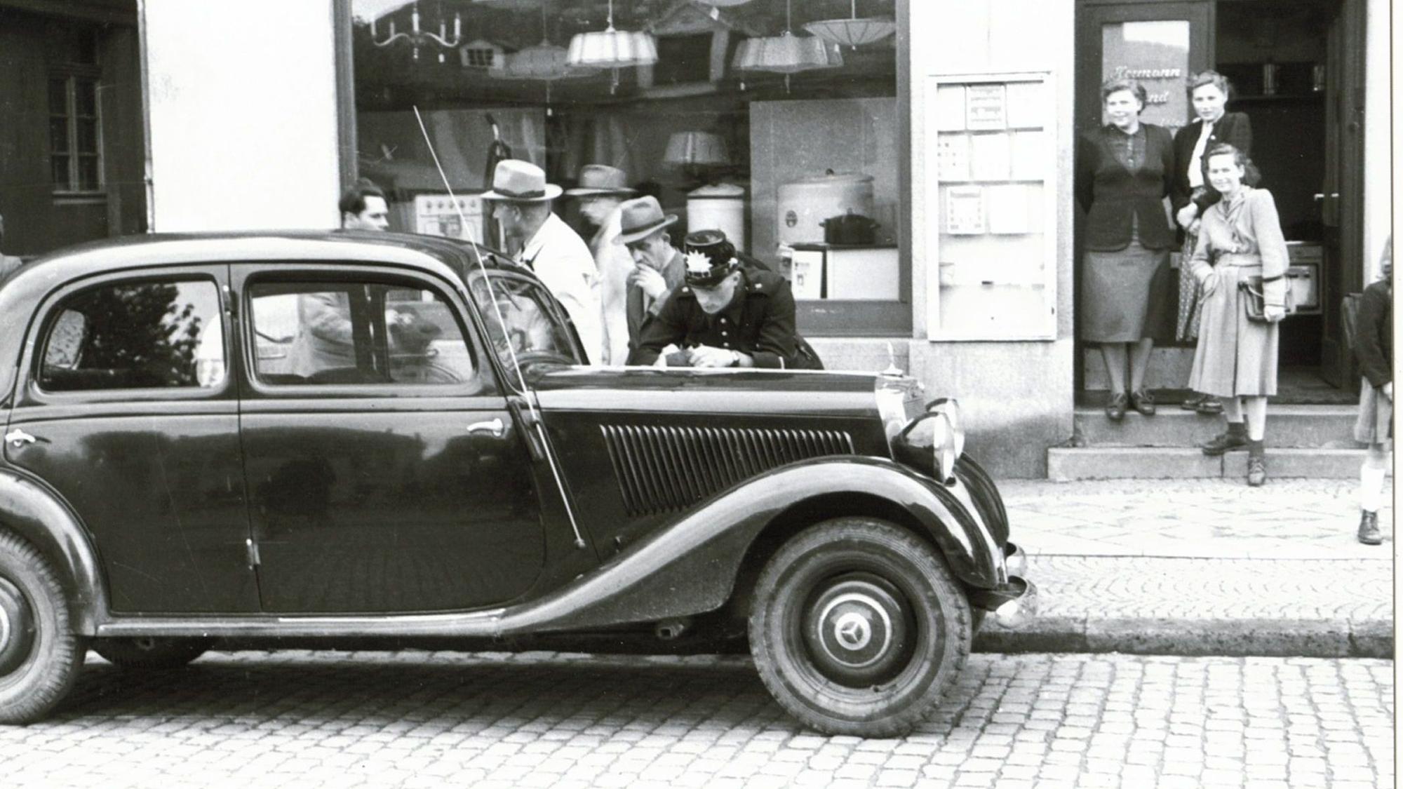 Ein Polizist schreibt auf der Motorhaube einer großen Limousine ein Strafmandat.
