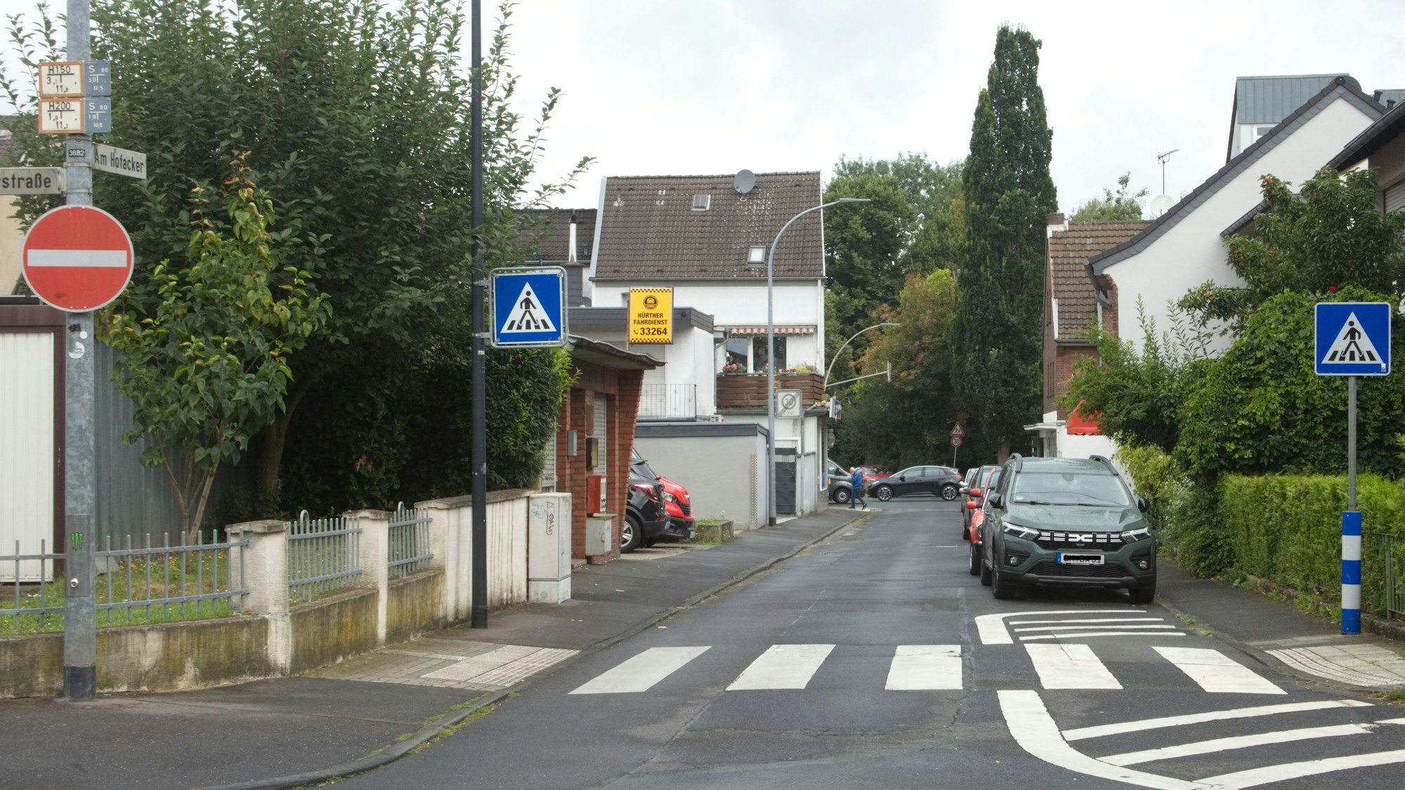 Eine schmale Straße, im Vordergrund ein Zebrastreifen, dahinter rechts Stellplätze.