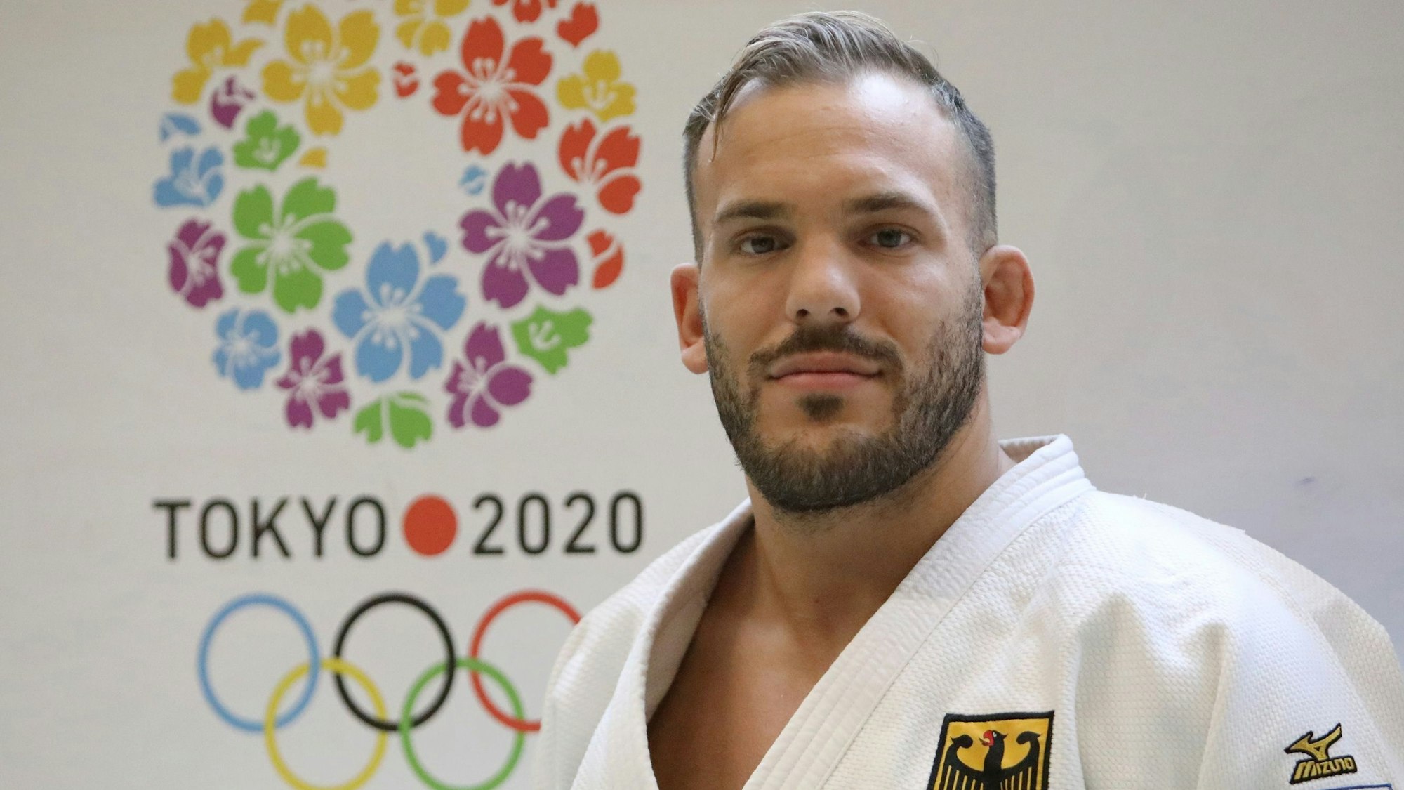 Portrait von Karl-Richard Frey vor einem Logo der Olympischen Spiele von Tokio.