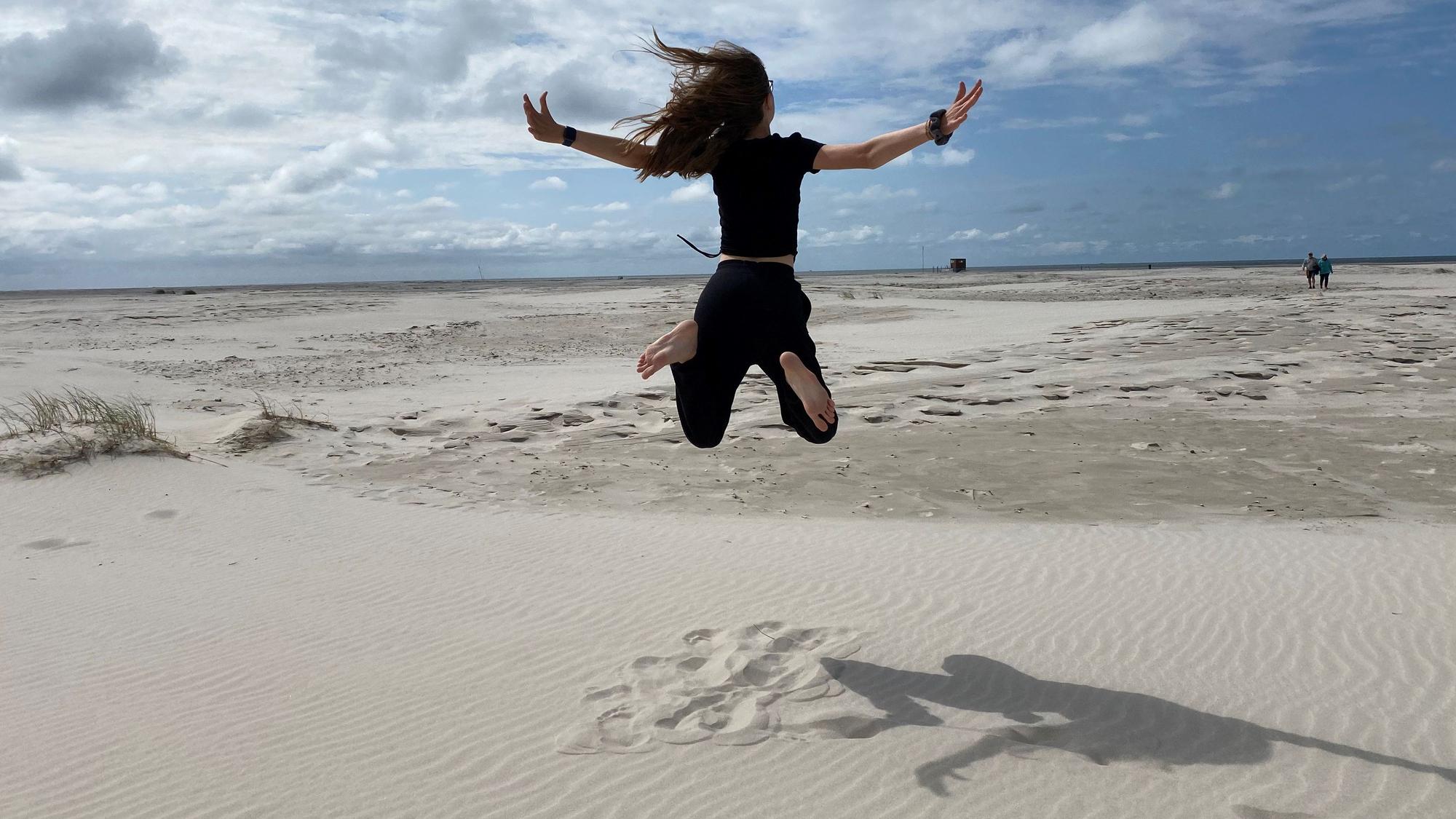 Das Bild zeigt ein Mädchen am Strand, das in die Luft springt.