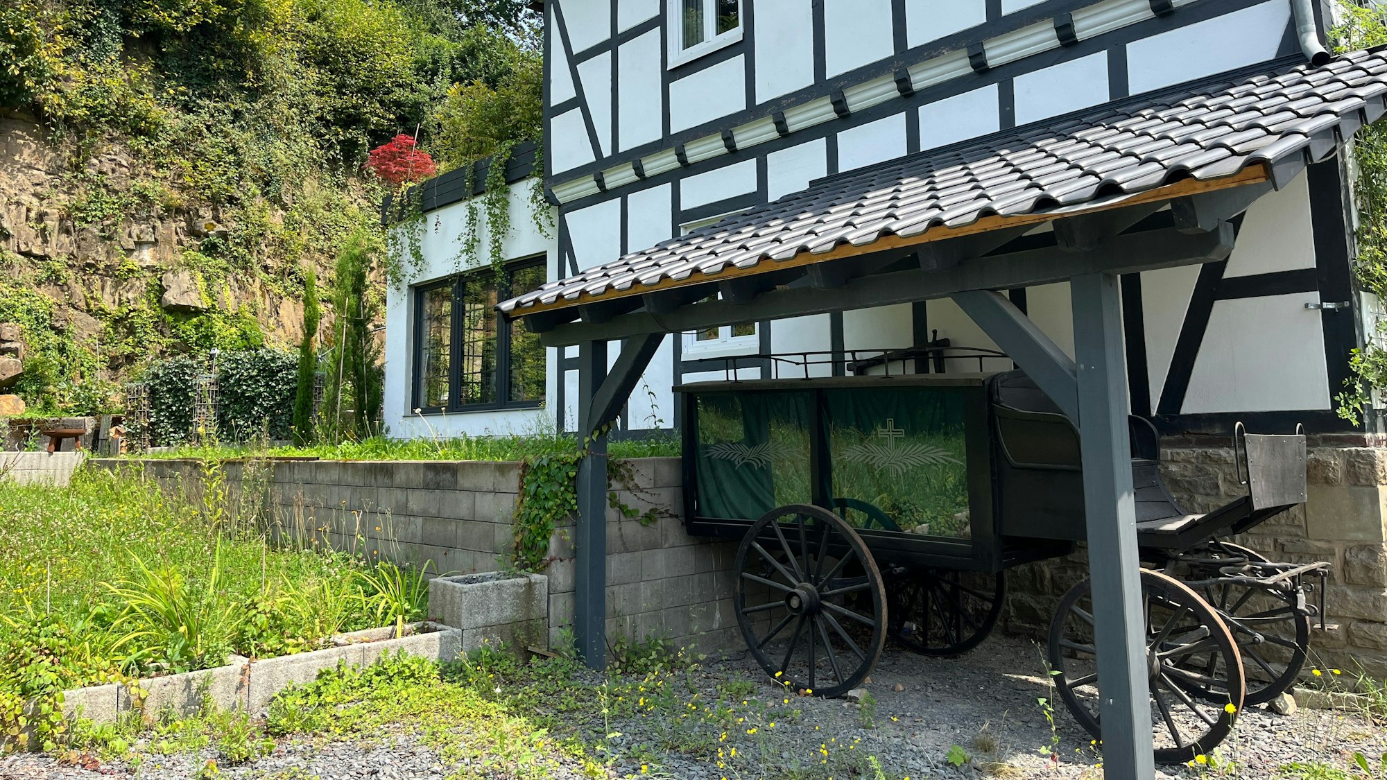 Im Unterstand ist ein schwarzer Bestattungswagen abgestellt.