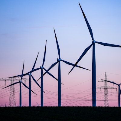 Windkraftanlagen und Hochspannungsleitungen sind vor dem Abendhimmel zu sehen. Zuletzt sorgte eine „Dunkelflaute“ für hohe Preise am Strommarkt. (Symbolbild)
