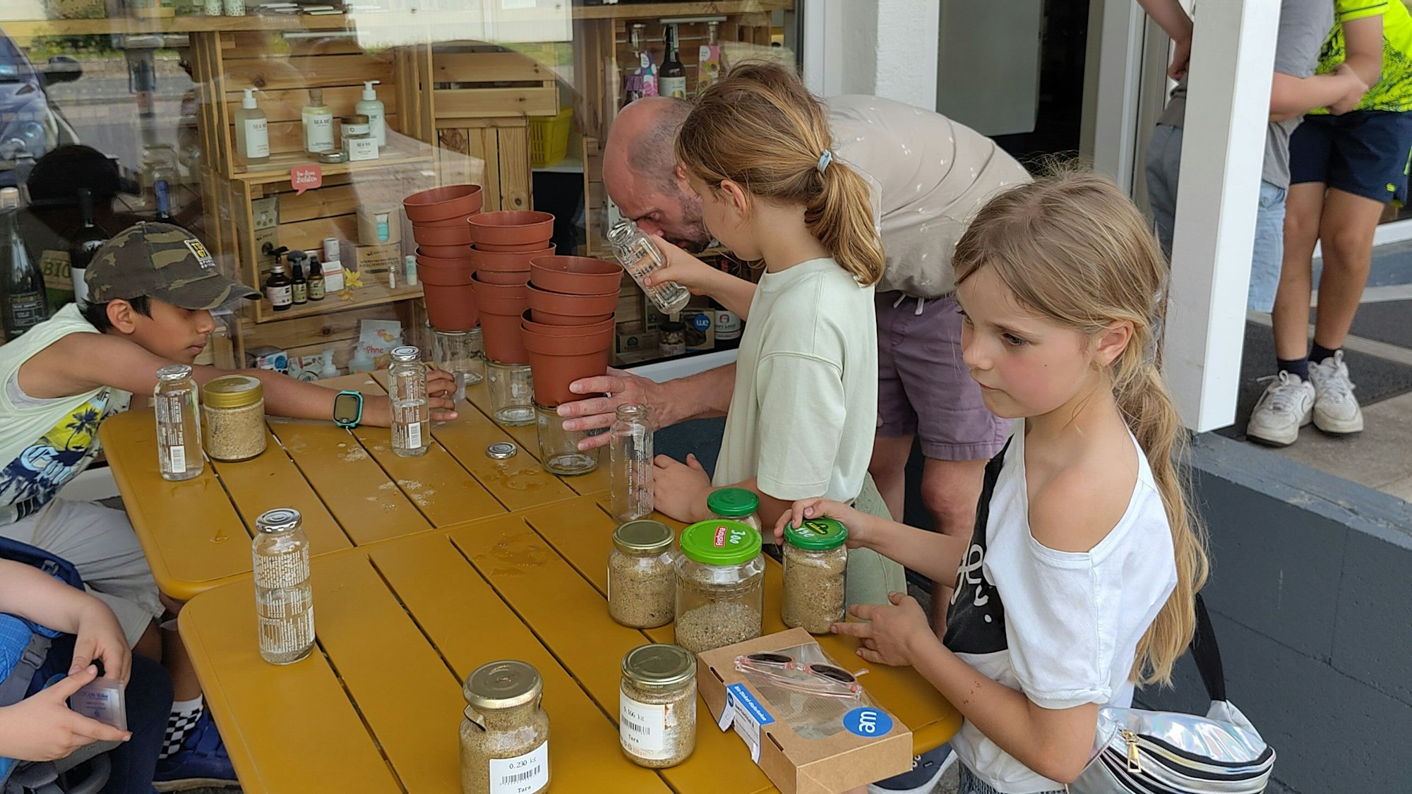 Kinder stehen und sitzen um einen Tisch, auf dem die Utensilien zum Wasser filtrieren stehen.