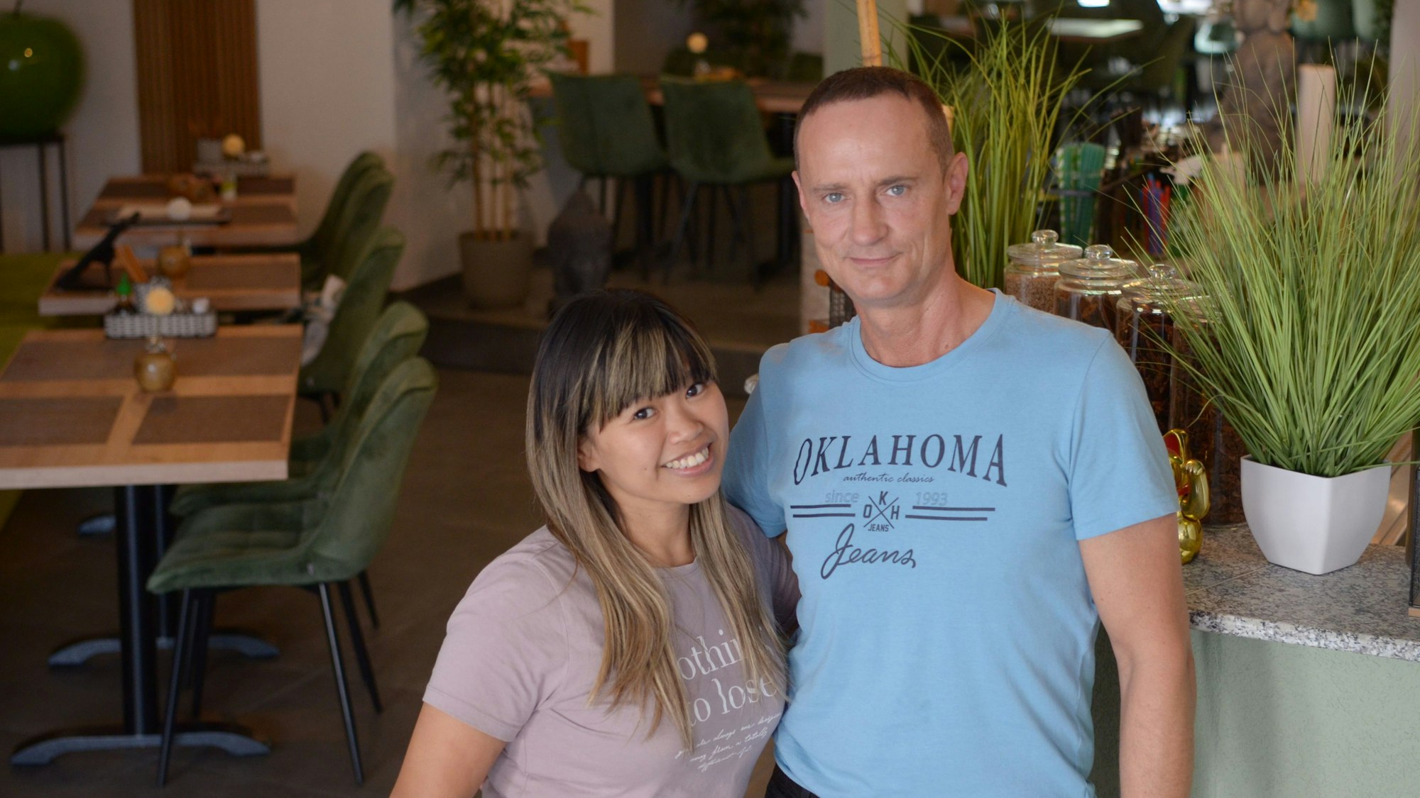 Thuy Tran und Dominik Fabrycki stehen nebeneinander in ihrem Restaurant, im Hintergrund Gästetische und die Getränketheke.