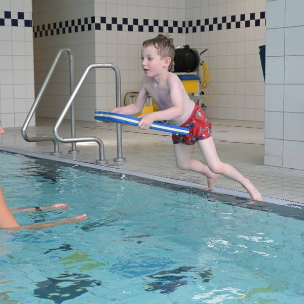 Adrian springt mit einem Schwimmbrett vom Beckenrand.