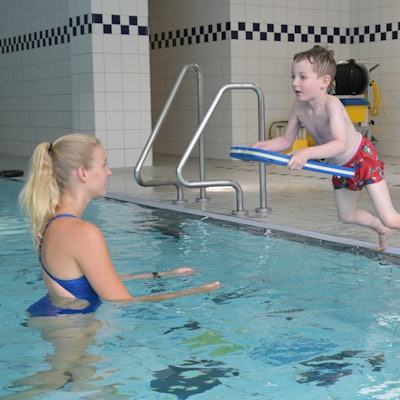 Adrian springt mit einem Schwimmbrett vom Beckenrand.