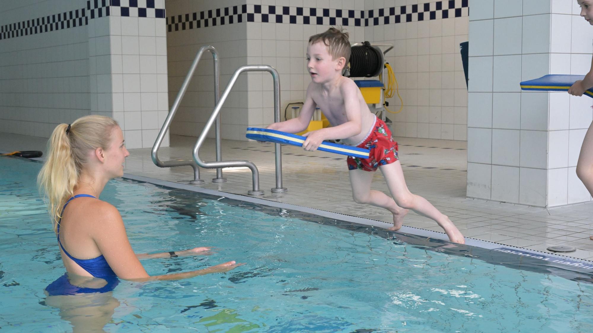 Adrian springt mit einem Schwimmbrett vom Beckenrand.