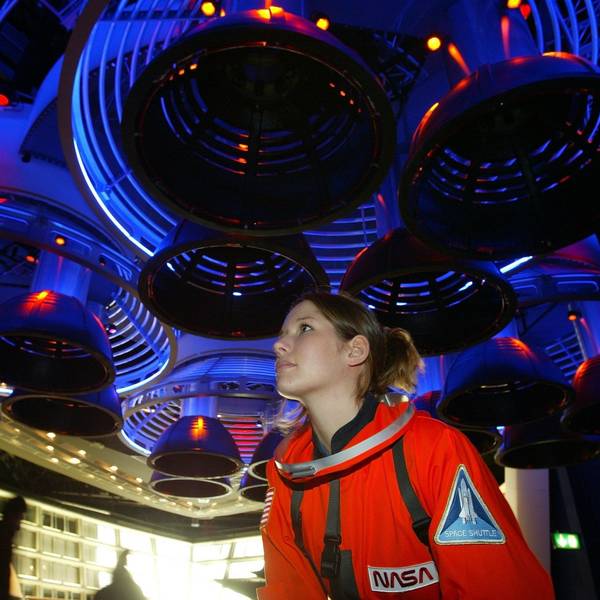 Fee Festersen steht in einem roten Astronauten-Anzug unter der Nachbildung von Raketentriebwerken.