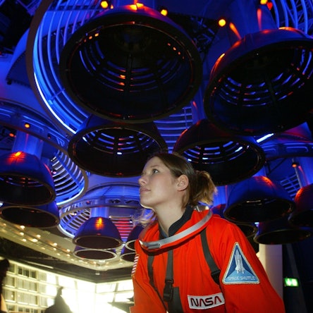 Fee Festersen steht in einem roten Astronauten-Anzug unter der Nachbildung von Raketentriebwerken.