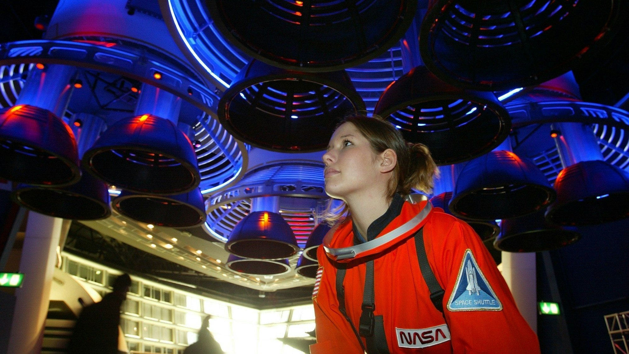 Fee Festersen steht in einem roten Astronauten-Anzug unter der Nachbildung von Raketentriebwerken.
