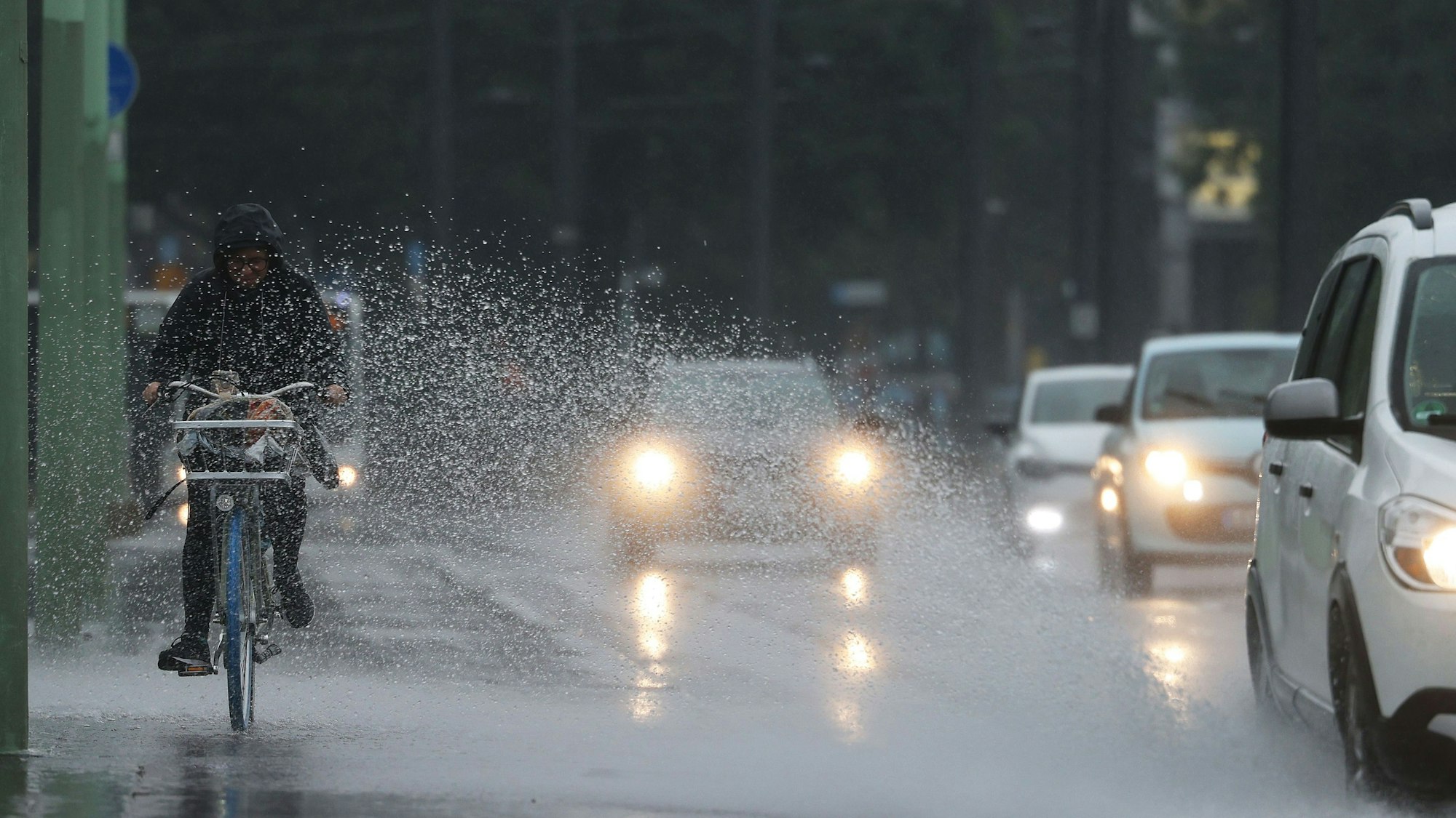 Eine Radfahrerin wird vom Spritzwasser eines Autos getroffen. In Nordrhein-Westfalen werden in den nächsten Tagen Gewitter und viel Regen erwartet.