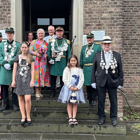 Männer und Frauen in Kleidern und Uniformen stehen vor einem Gebäude.