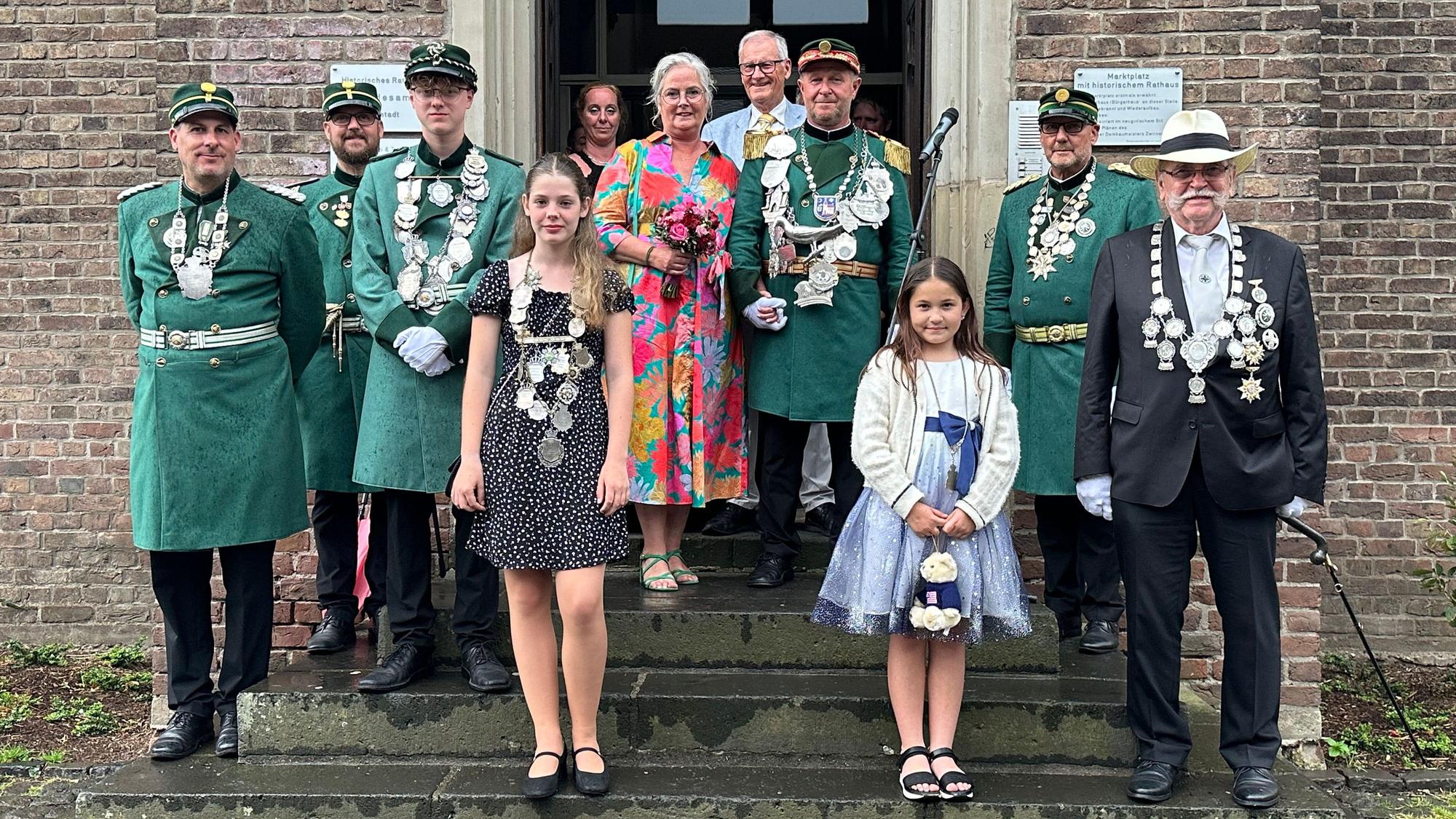 Männer und Frauen in Kleidern und Uniformen stehen vor einem Gebäude.
