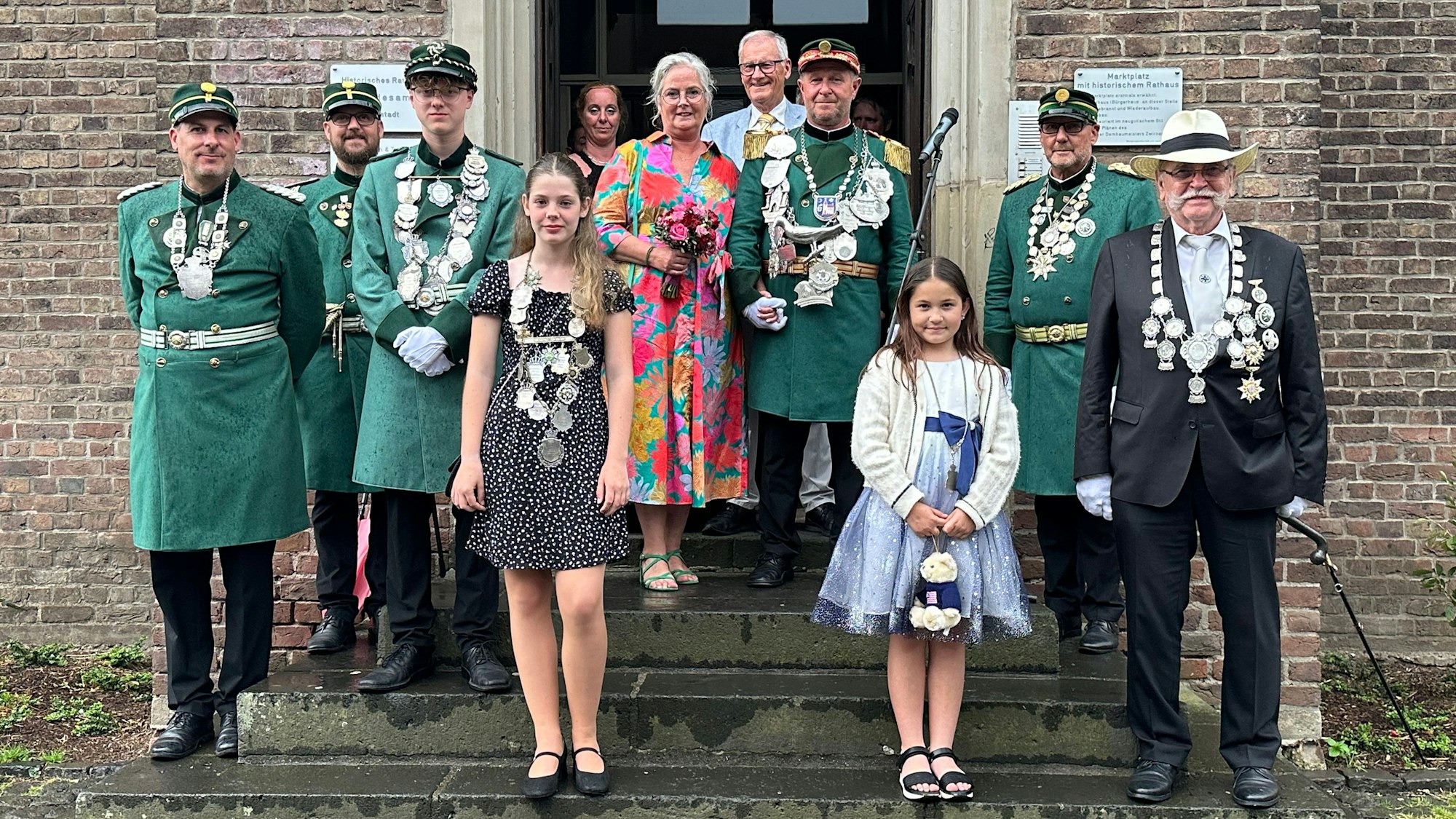 Männer und Frauen in Kleidern und Uniformen stehen vor einem Gebäude.