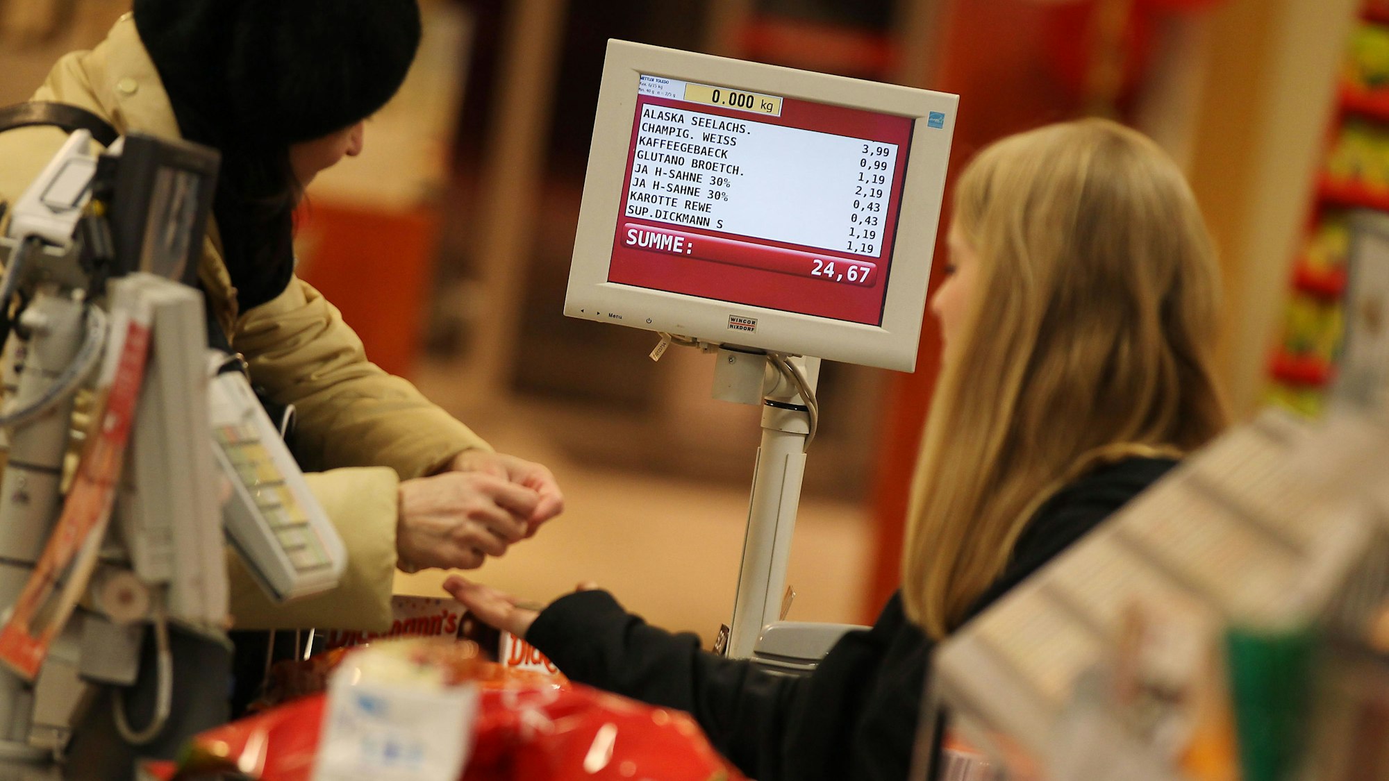 ARCHIV - Ein Kassiererin nimmt am 13.02.2012 in Köln (Nordrhein-Westfalen) in einem Rewe-Supermarkt das Geld einer Kundin entgegen. Foto: Oliver Berg/dpa (zu dpa "In Rewe-Supermärkten klingeln die Kassen" vom 31.03.2015) +++ dpa-Bildfunk +++