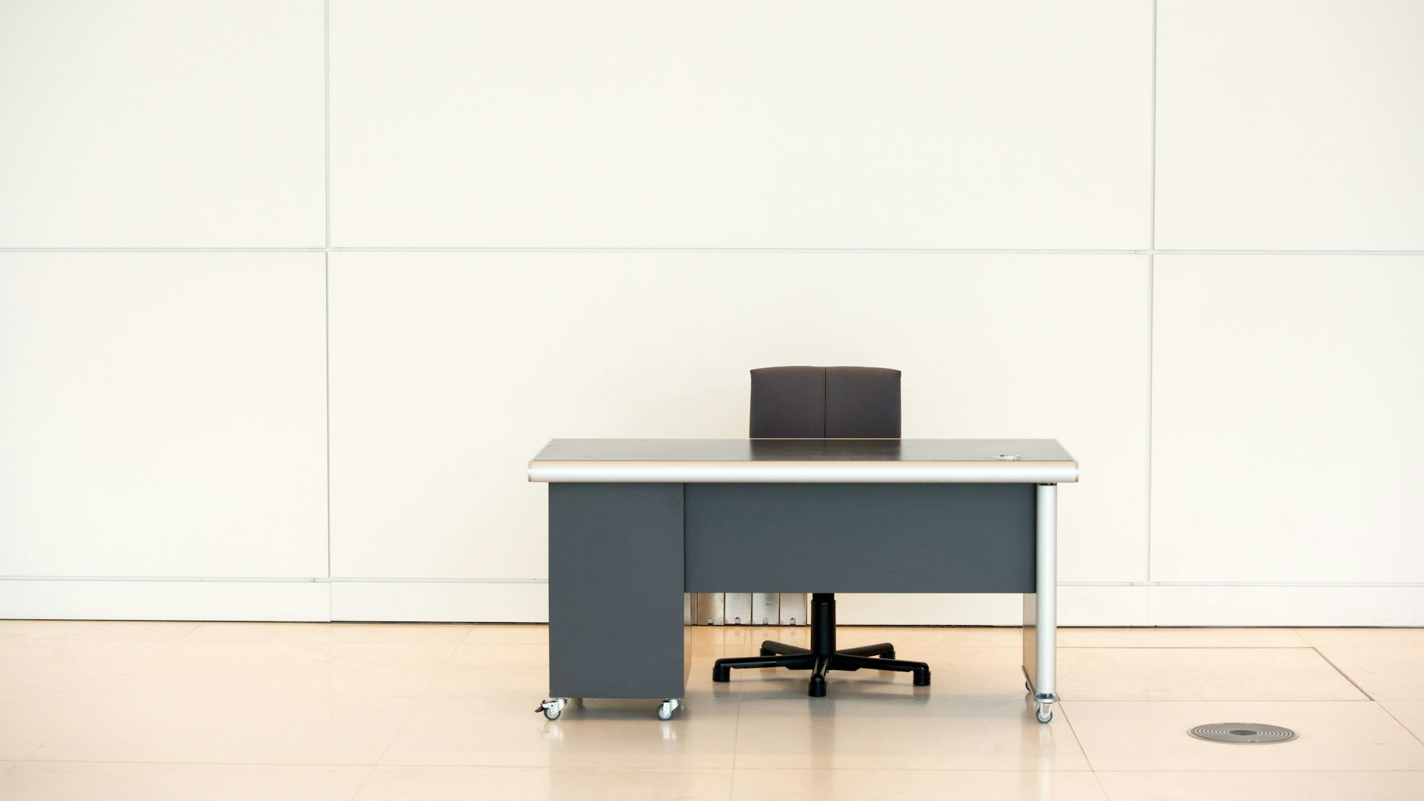 Ein leerer Schreibtisch und ein Bürostuhl stehen vor einer Wand.