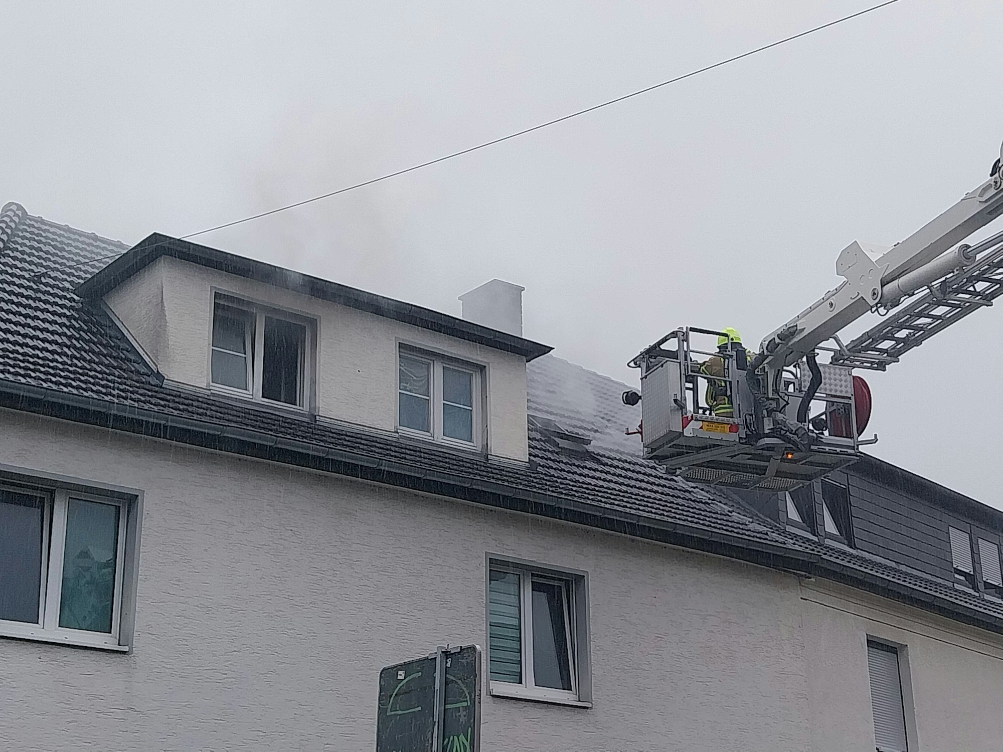 Rauch steigt aus Fenstern empor, daneben ein Korb einer Drehleiter.