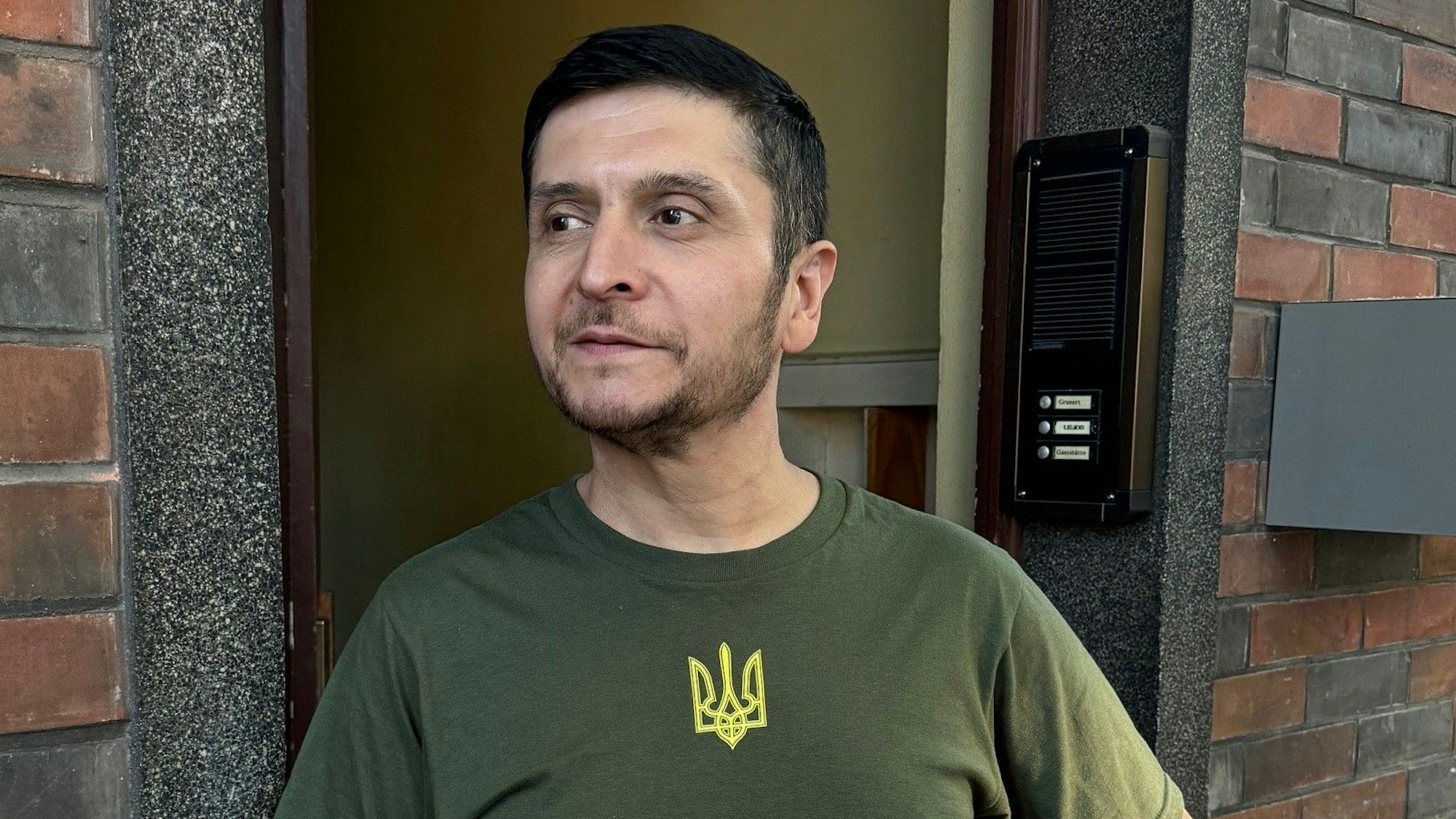 Das Selenskyj-Double Umid Isabaev aus Usbekistan steht an einer Haustüre vor einer Stadt im Ruhrgebiet. Ihm droht die Abschiebung.