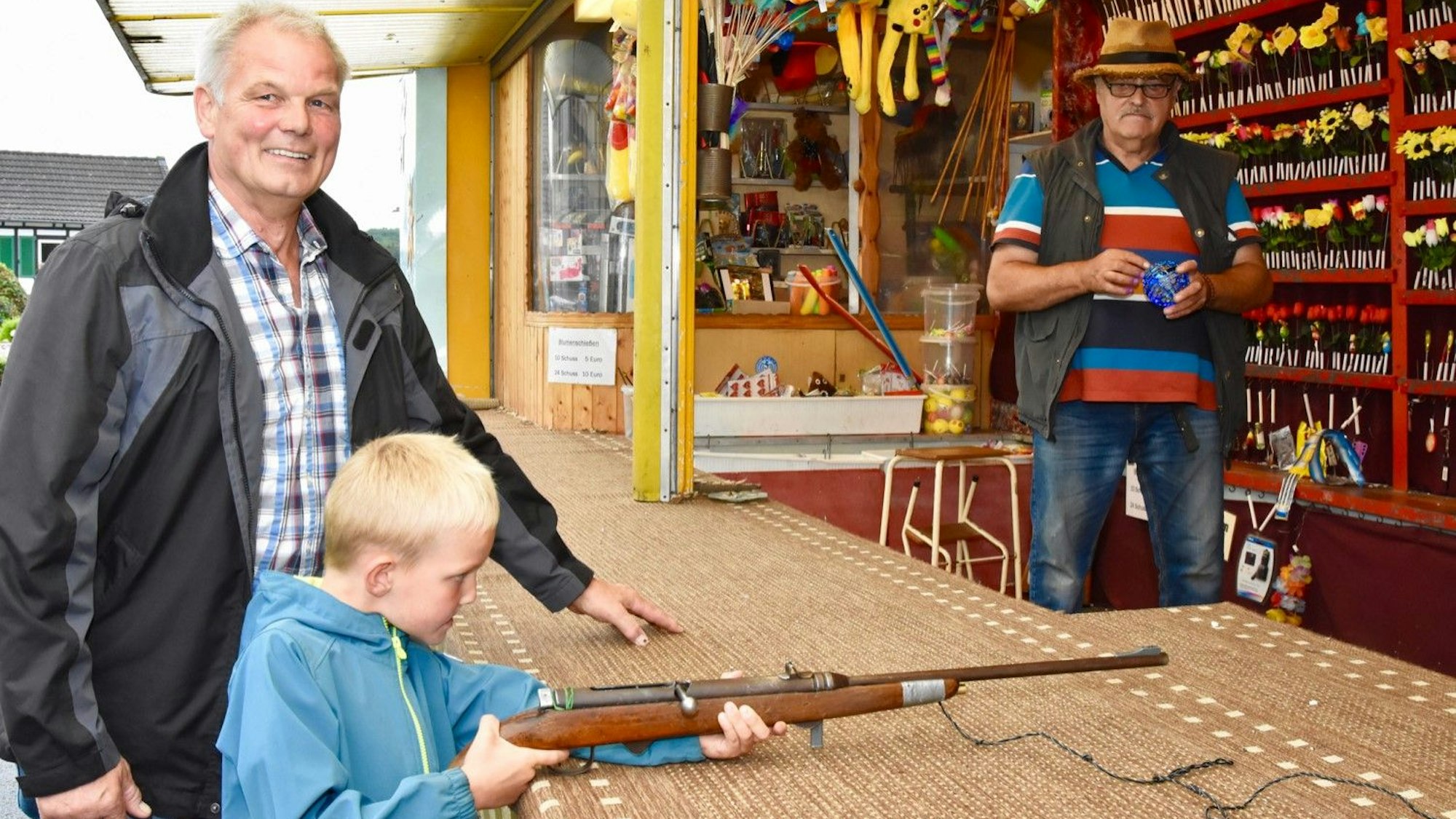 Eine Schießbude auf einer Dorfkirmes. Ein kleinerJunge legt auf sein Ziel an.