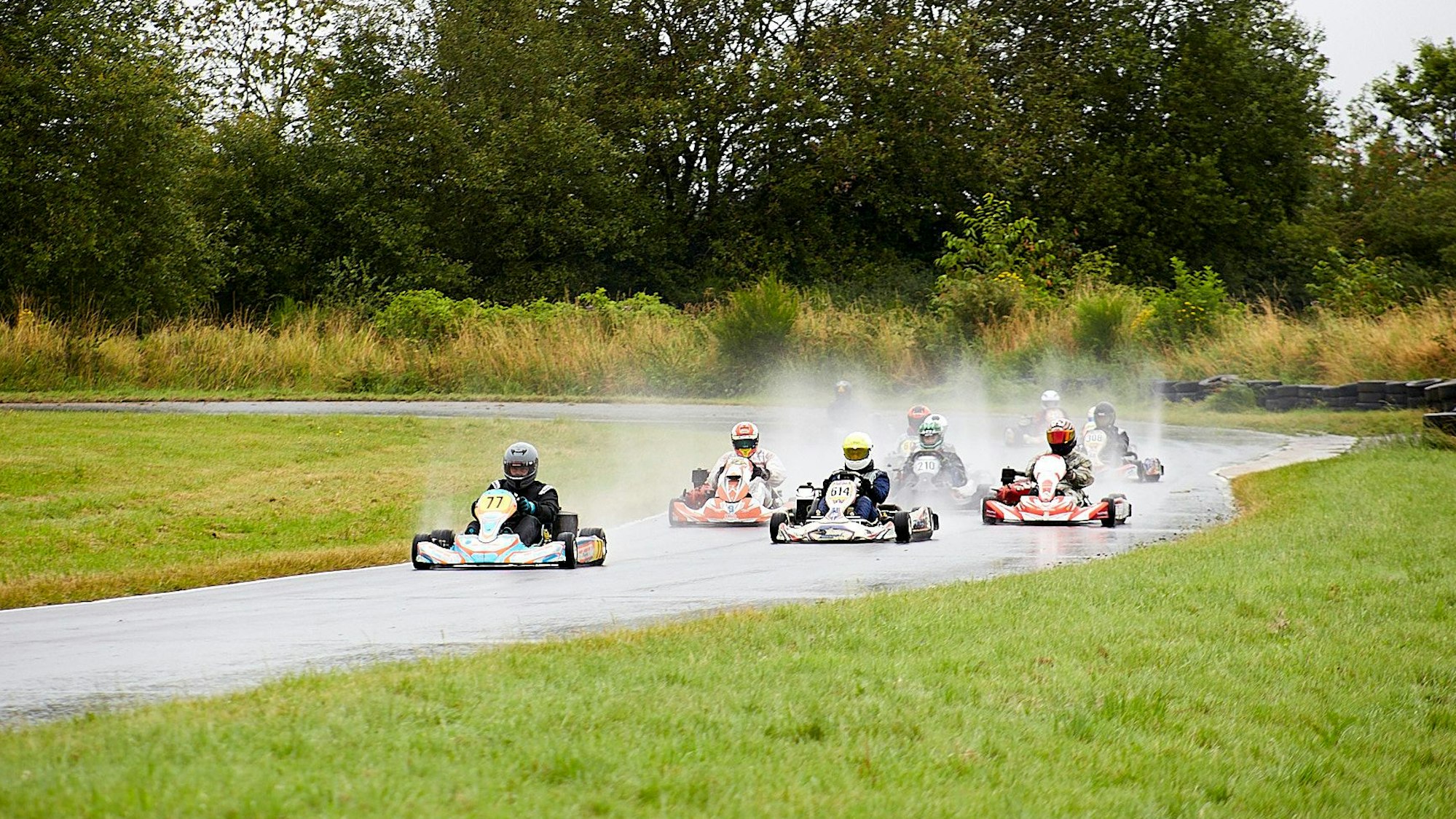 Mehrere Karts fahren hintereinander, das Wasser von der Strecke spritzt hoch.