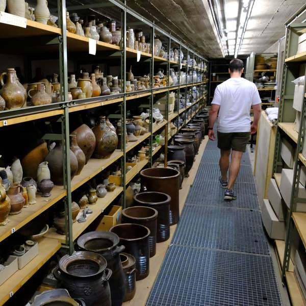 Töpferwaren aus dem Rheinland lagern in Regalen des Kommerner Museums-Depots. Ein Mitarbeiter geht daran vorbei.