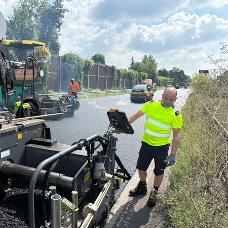 Arbeiter bringen Asphalt auf einer Straße auf.
