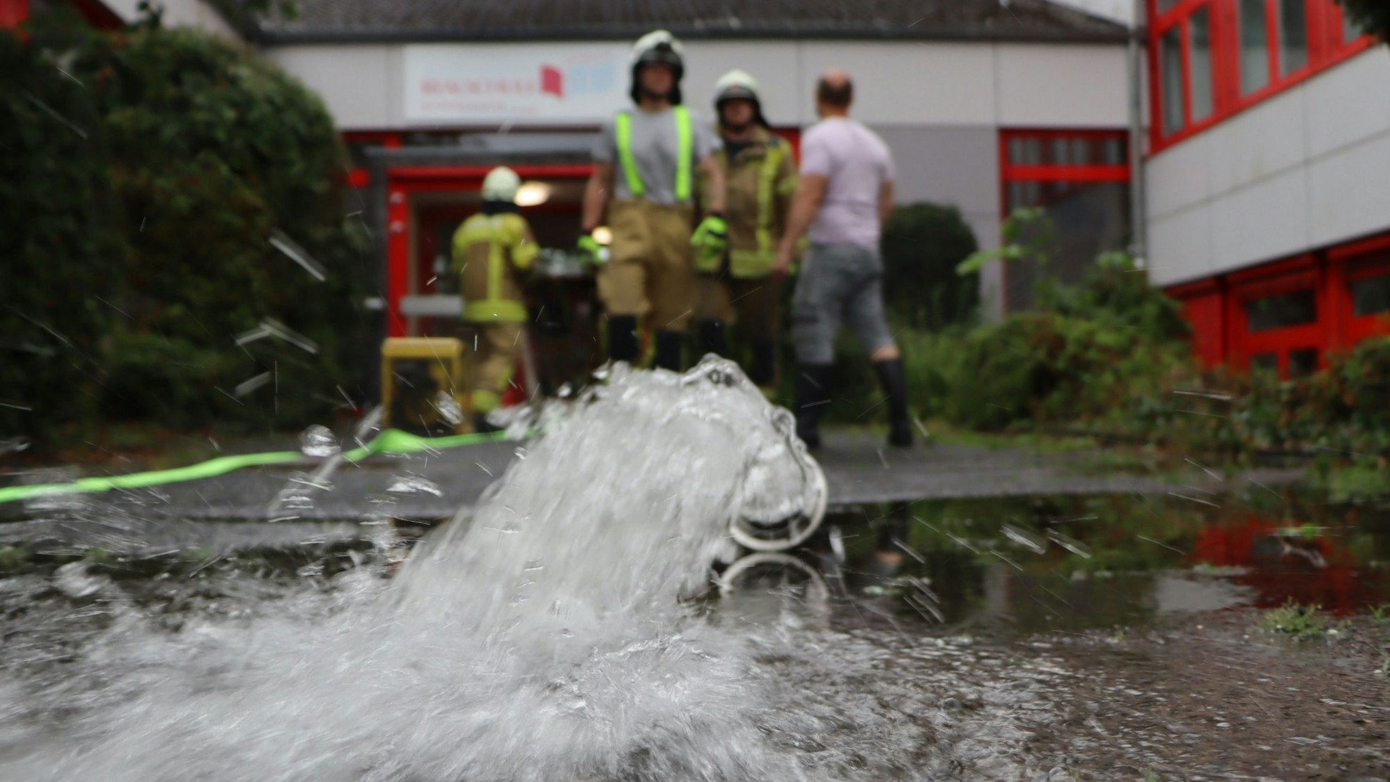 Zu sehen ist ein Wasserschlauch der Feuerwehr vor einem Gebäude. .