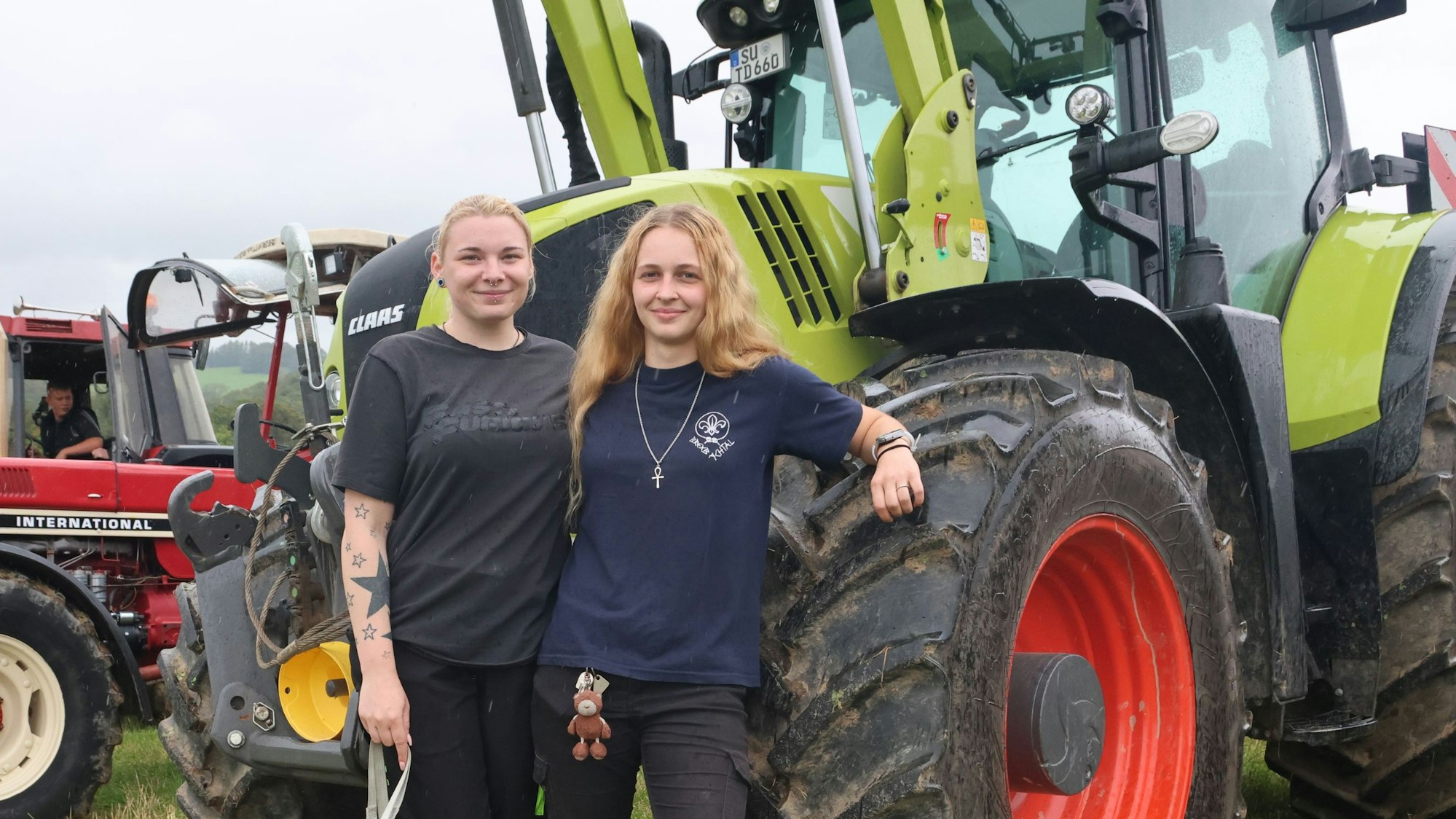 Das Foto zeigt zwei junge Frauen und Trecker im Hintergrund.