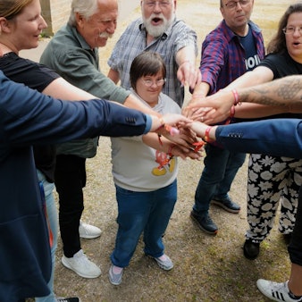 Männer und Frauen haben einen Kreis gebildet und berühren sich in der Mitte an den Händen.