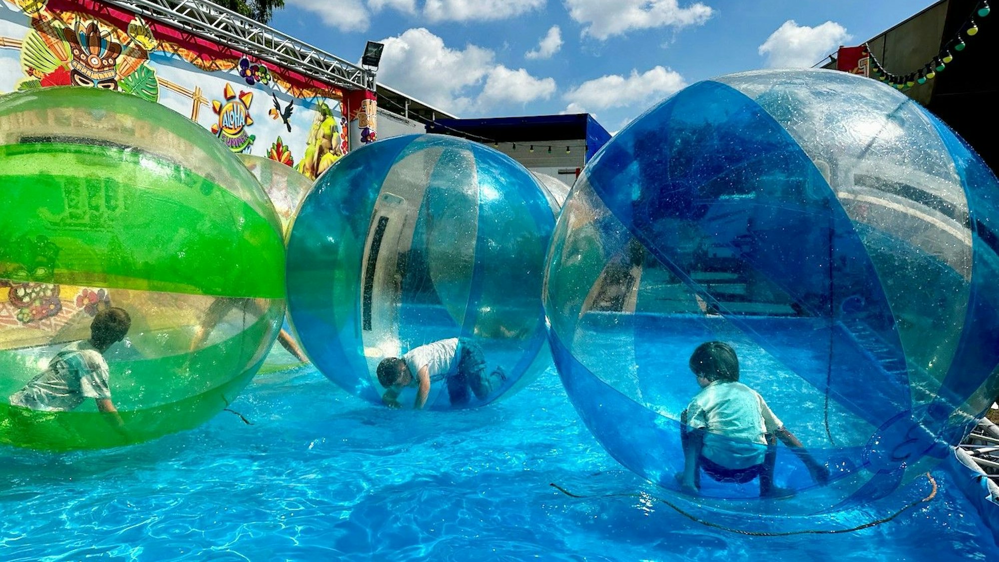 Kinder spielen in durchsichtigen Bällen in einem Wasserbecken.